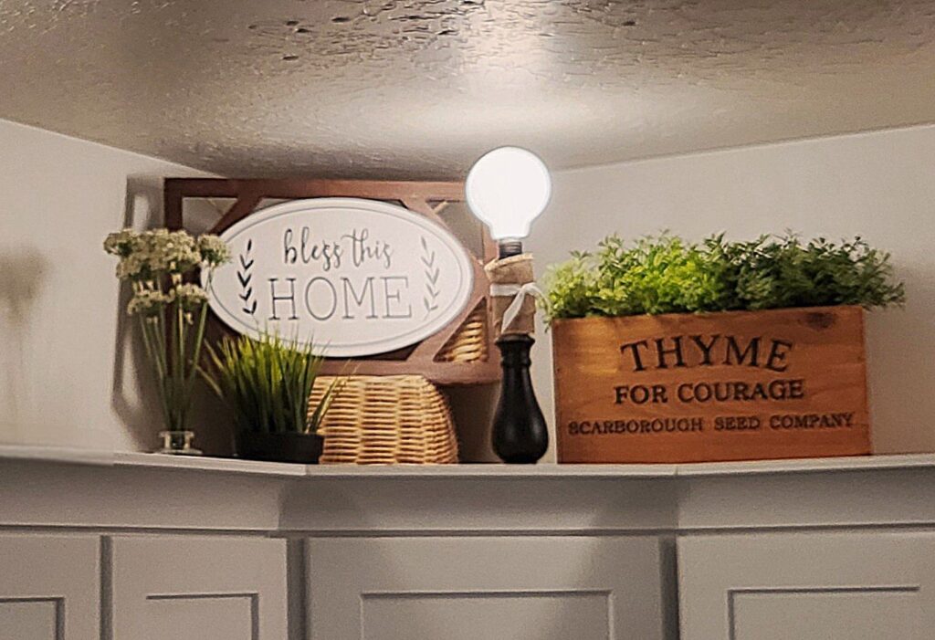 A wooden box of herbs grouped with more greens, wicker baskets, and a thrifted lamp and wall hanging.