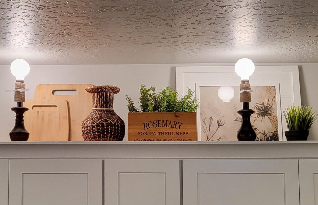 Glorious grouping of lamps, cutting boards, and a picture frame with repurposed-pillow-case art. All from the thrift store! With wicker, and greenery added.